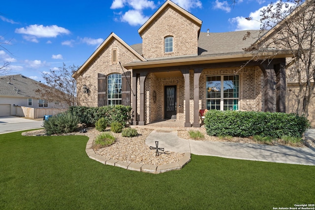 view of front of home featuring covered porch, a shingled roof, a front lawn, and brick siding