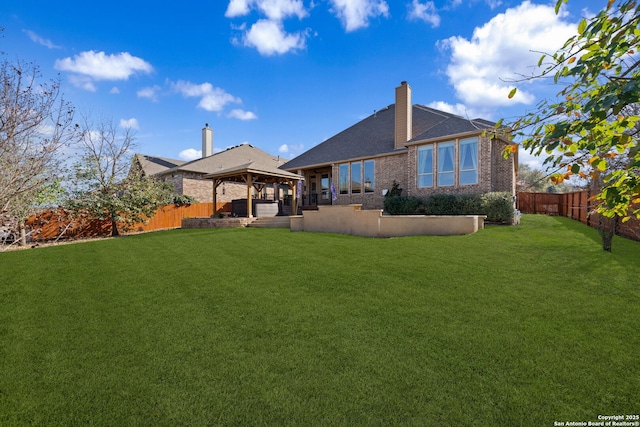 rear view of house featuring a gazebo, a lawn, a chimney, and a fenced backyard