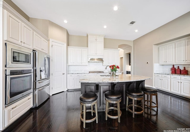 kitchen featuring under cabinet range hood, visible vents, white cabinets, appliances with stainless steel finishes, and a center island with sink