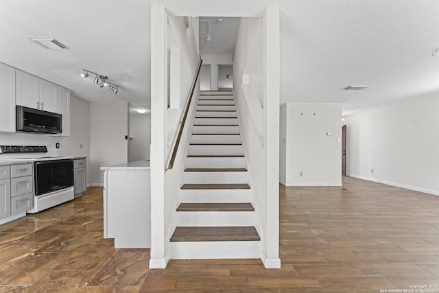 stairway featuring wood-type flooring, a textured ceiling, and track lighting