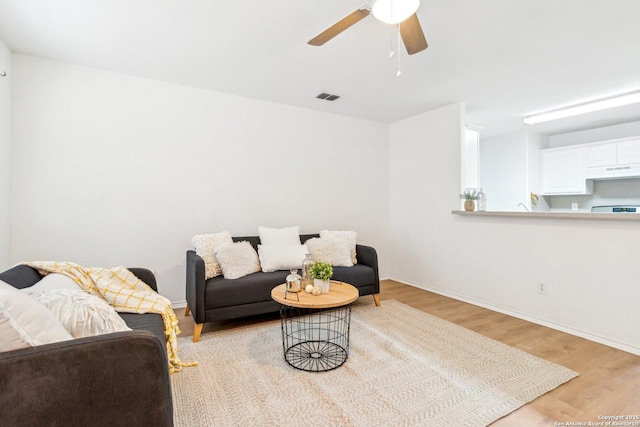 living area with light wood-type flooring, visible vents, ceiling fan, and baseboards