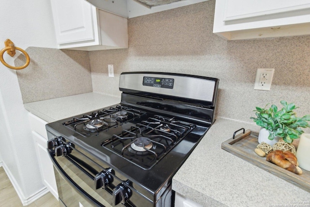 kitchen featuring white cabinets, light countertops, decorative backsplash, range hood, and gas range