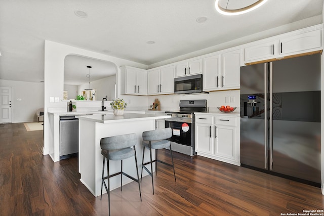 kitchen featuring dark hardwood / wood-style flooring, kitchen peninsula, pendant lighting, stainless steel appliances, and white cabinets