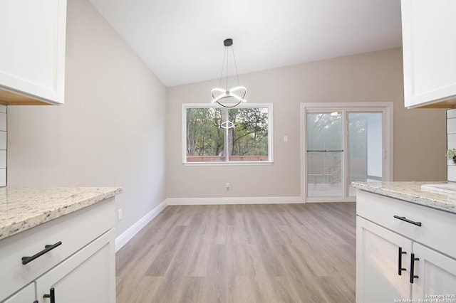 unfurnished dining area with vaulted ceiling, a chandelier, and light wood-type flooring