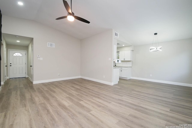 unfurnished living room featuring vaulted ceiling, ceiling fan with notable chandelier, and light hardwood / wood-style floors