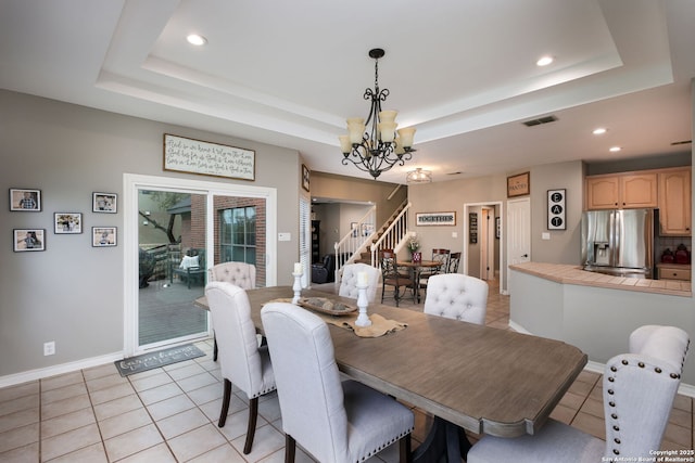 tiled dining area with a raised ceiling and a chandelier