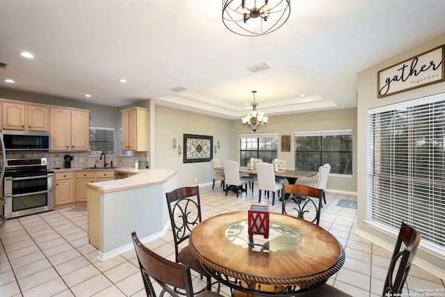 dining area featuring light brown cabinetry, sink, an inviting chandelier, decorative light fixtures, and a raised ceiling