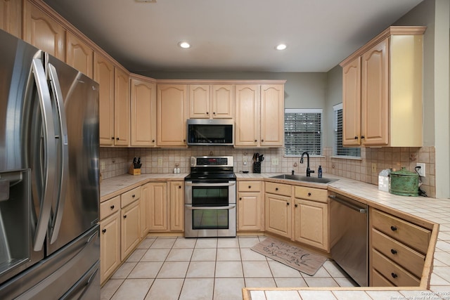 kitchen featuring light brown cabinetry, sink, tile countertops, appliances with stainless steel finishes, and backsplash