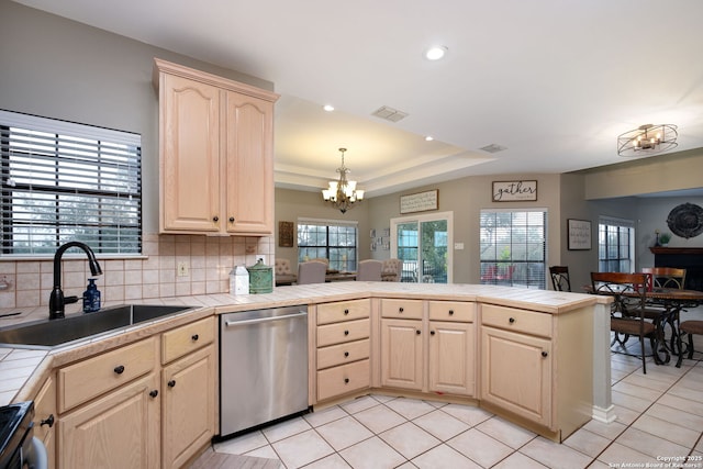 kitchen featuring tile countertops, light brown cabinetry, sink, stainless steel dishwasher, and a tray ceiling