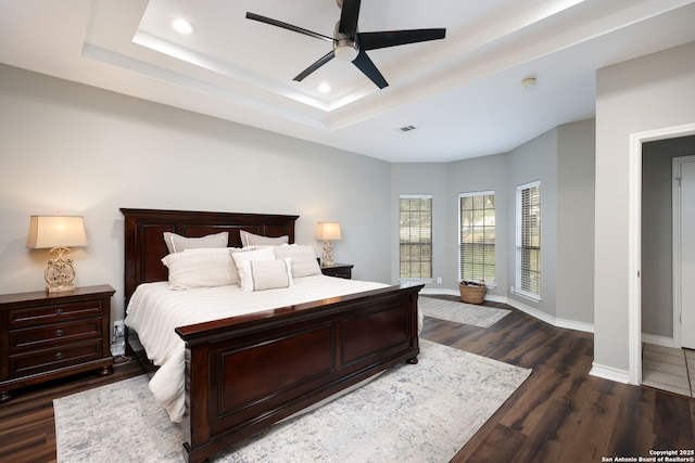 bedroom featuring dark hardwood / wood-style floors, ceiling fan, and a tray ceiling