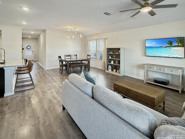 living room featuring ceiling fan with notable chandelier and dark wood-type flooring