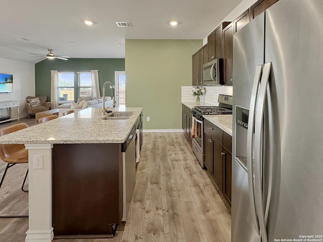 kitchen with sink, a breakfast bar area, a kitchen island with sink, stainless steel appliances, and light wood-type flooring