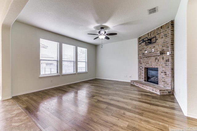 unfurnished living room featuring ceiling fan, a fireplace, hardwood / wood-style floors, and a textured ceiling