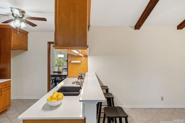 kitchen featuring light tile patterned flooring, a breakfast bar, sink, ceiling fan, and beam ceiling