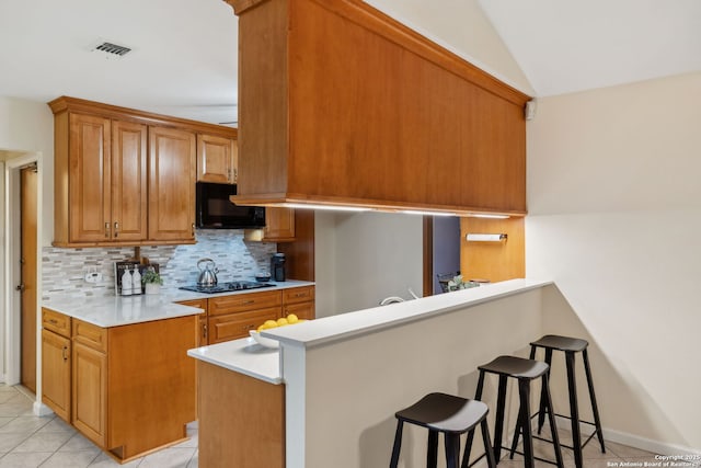 kitchen with light tile patterned flooring, kitchen peninsula, a breakfast bar area, and backsplash