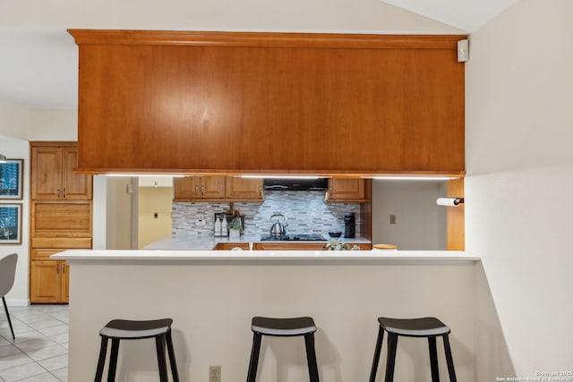 kitchen featuring a kitchen bar, light tile patterned floors, kitchen peninsula, stainless steel gas stovetop, and backsplash