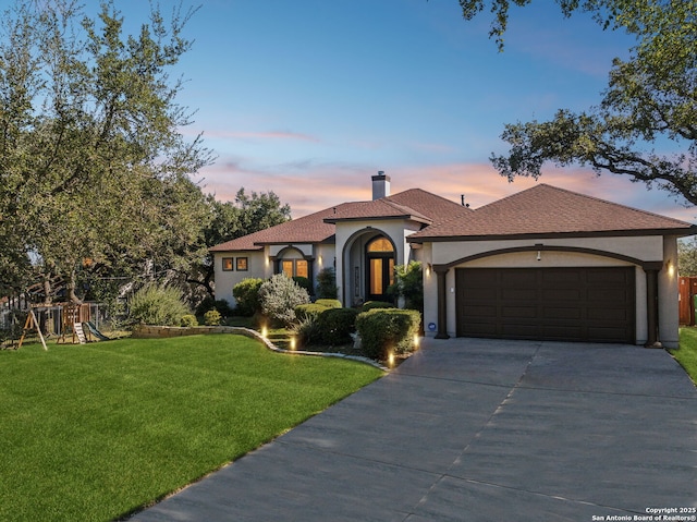 mediterranean / spanish home featuring a playground, a garage, and a lawn