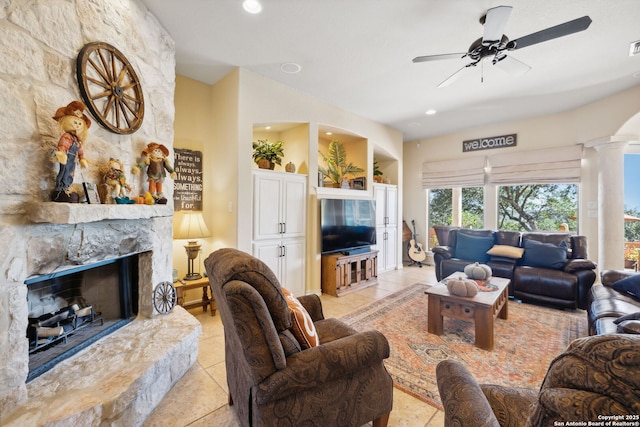 living room featuring light tile patterned floors, a stone fireplace, decorative columns, and ceiling fan