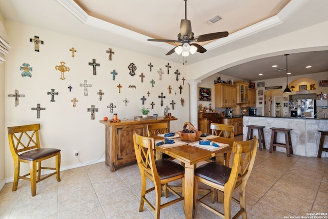 tiled dining room with crown molding, decorative columns, a raised ceiling, and ceiling fan