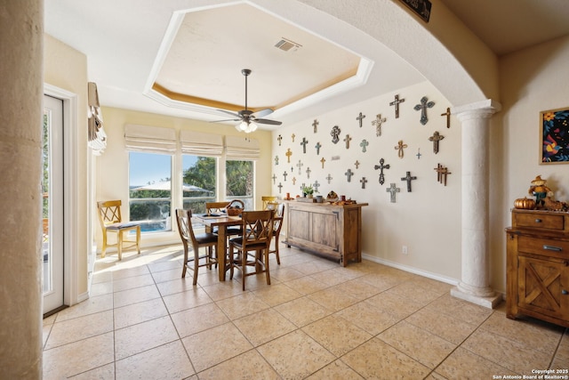 tiled dining area featuring ceiling fan, a tray ceiling, and decorative columns