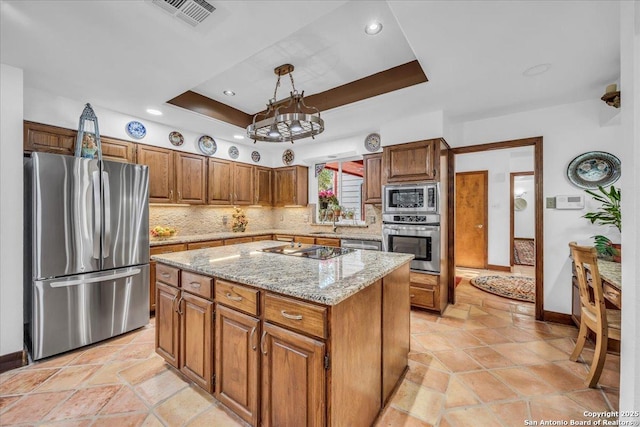 kitchen with appliances with stainless steel finishes, hanging light fixtures, tasteful backsplash, a tray ceiling, and a kitchen island