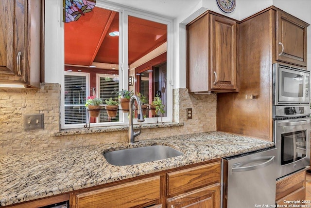 kitchen with appliances with stainless steel finishes, light stone countertops, sink, and decorative backsplash