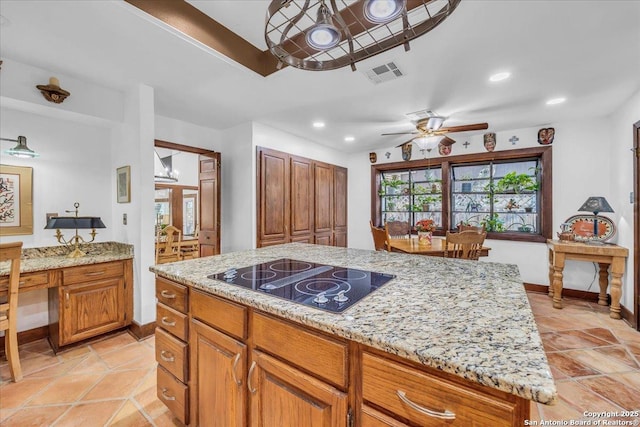 kitchen with built in desk, a center island, ceiling fan, light stone counters, and black electric cooktop