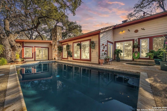 pool at dusk featuring a hot tub