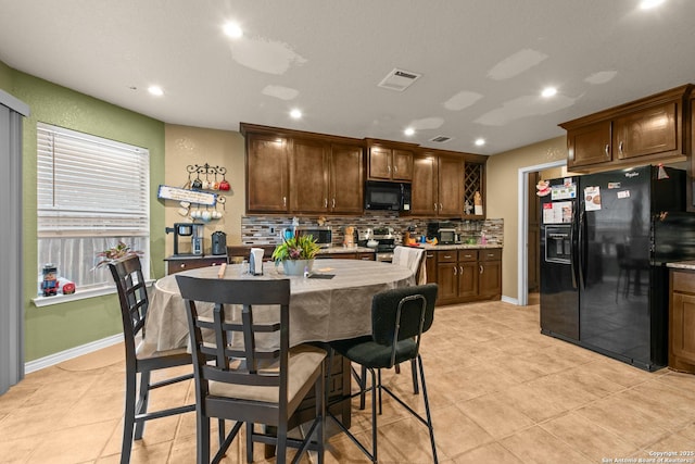 kitchen with tasteful backsplash, light tile patterned flooring, black appliances, and a center island with sink