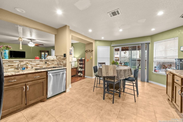 kitchen featuring tasteful backsplash, light stone countertops, stainless steel dishwasher, and sink