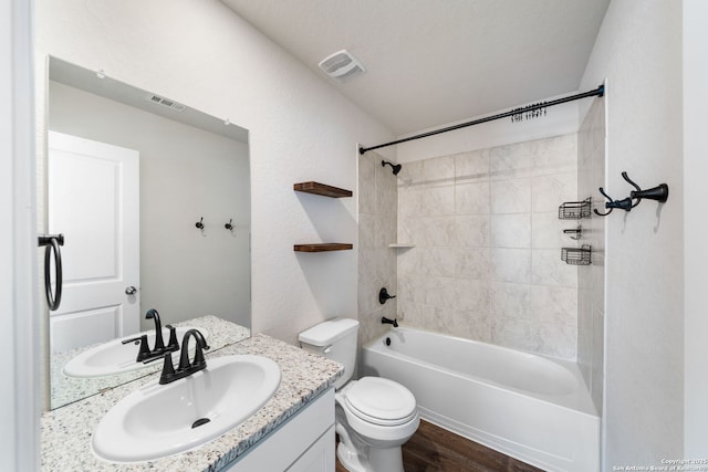 full bathroom featuring vanity, hardwood / wood-style floors, tiled shower / bath combo, and toilet