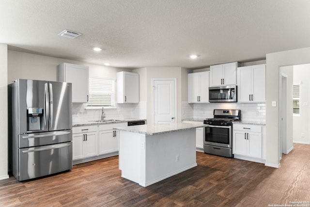 kitchen with a kitchen island, appliances with stainless steel finishes, white cabinetry, sink, and light stone counters