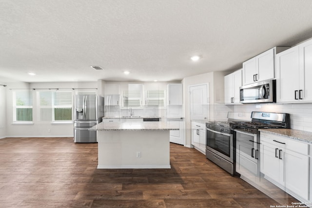 kitchen featuring dark wood-type flooring, white cabinetry, a center island, stainless steel appliances, and light stone countertops