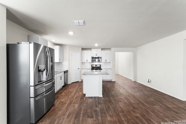 kitchen featuring white cabinets, decorative backsplash, a center island, stainless steel appliances, and dark wood-type flooring