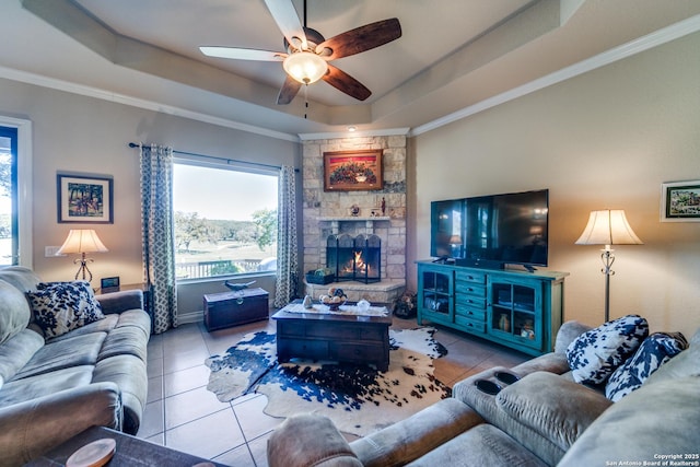 living room with crown molding, a tray ceiling, a fireplace, and light tile patterned flooring