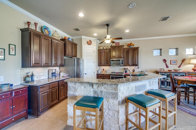 kitchen with a kitchen island with sink, light stone counters, a breakfast bar area, and appliances with stainless steel finishes