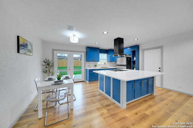 kitchen featuring sink, blue cabinetry, island exhaust hood, french doors, and light wood-type flooring