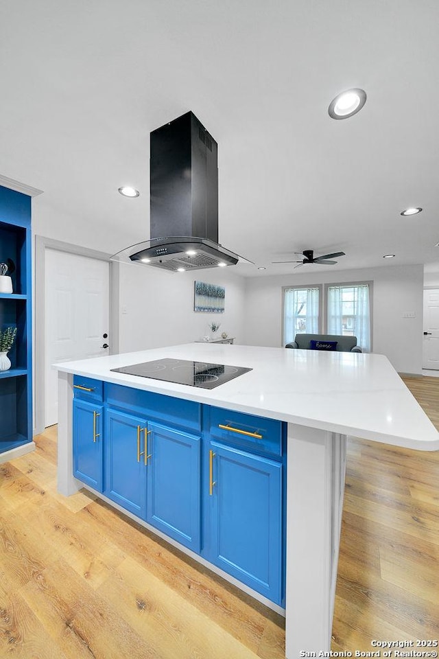 kitchen with blue cabinetry, island exhaust hood, black electric cooktop, and light hardwood / wood-style floors