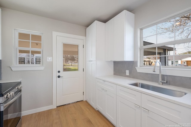 kitchen featuring stainless steel electric range oven, sink, backsplash, white cabinets, and light hardwood / wood-style floors