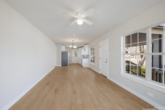 unfurnished living room featuring ceiling fan with notable chandelier and light hardwood / wood-style floors