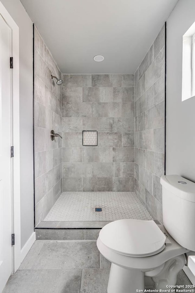 bathroom with a tile shower and toilet