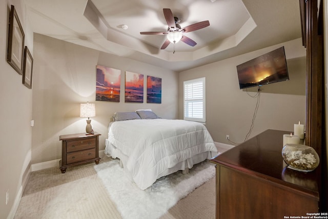 bedroom featuring a raised ceiling, light carpet, and ceiling fan