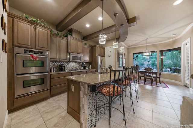 kitchen featuring a kitchen island with sink, decorative light fixtures, stainless steel appliances, and dark stone countertops