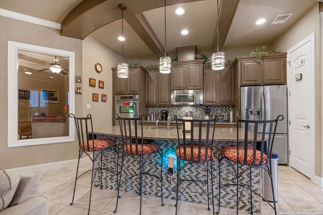 kitchen with decorative light fixtures, appliances with stainless steel finishes, an island with sink, dark stone counters, and beam ceiling