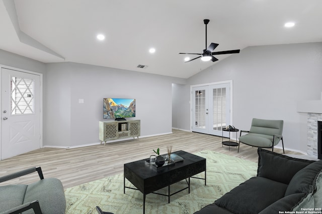 living room with vaulted ceiling, a stone fireplace, french doors, ceiling fan, and light hardwood / wood-style flooring