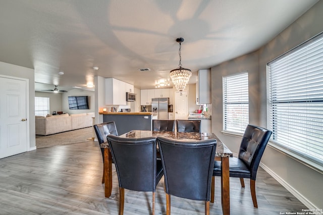 dining area with wood-type flooring and ceiling fan with notable chandelier