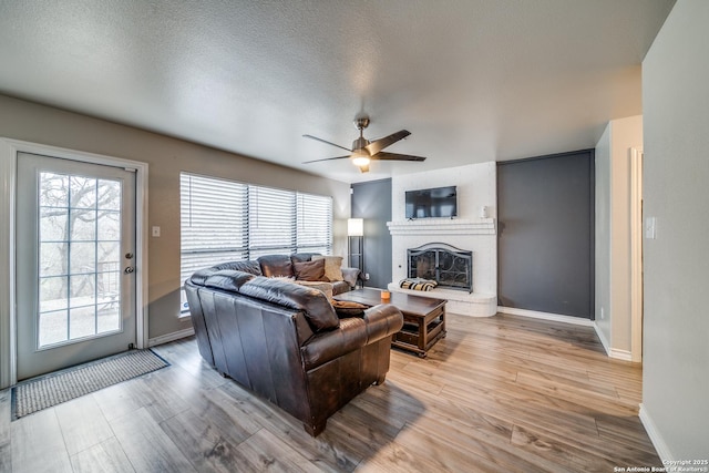 living room with a brick fireplace, light hardwood / wood-style flooring, a healthy amount of sunlight, and ceiling fan