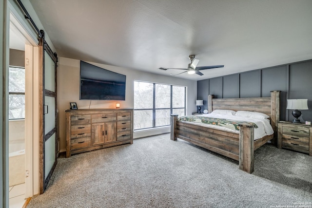 carpeted bedroom with ceiling fan and a barn door