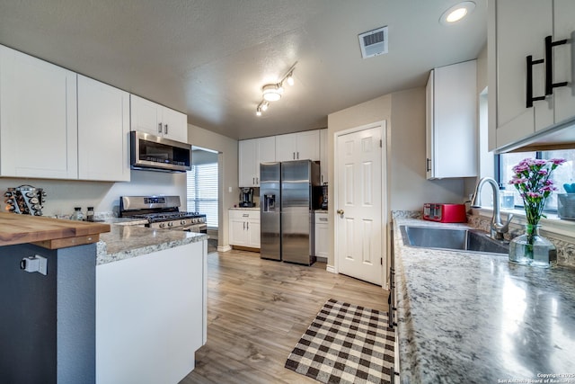 kitchen featuring butcher block countertops, sink, appliances with stainless steel finishes, white cabinets, and light wood-type flooring