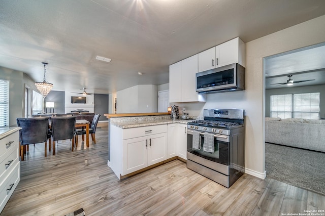 kitchen with appliances with stainless steel finishes, hanging light fixtures, a wealth of natural light, white cabinets, and kitchen peninsula